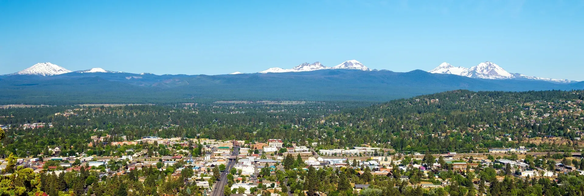 A city in Oregon with Mountain views on a blue sky day - lots of trees in the city.